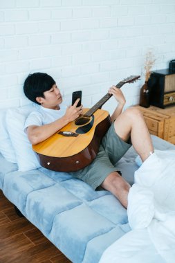 Yalan söylerken gitar çalan siyah saçlı müzisyen. Beyaz yatakta, yatak odasında..