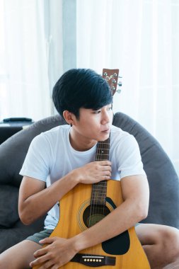 Siyah saçlı müzisyen siyah armut çantasına oturup gitarını kucaklıyor..