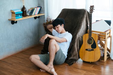 Siyah saçlı müzisyen, tahta zeminde oturmuş kahverengi sandalyeye yaslanıyor..