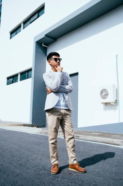 Genç adam beyaz binanın önünde duran güçlü güneş ışığında iş adamı gibi görünüyor..