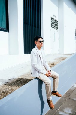 Yazın bir binanın yamacında oturan sıradan görünümlü genç adam..