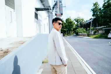 Beyaz takım elbiseli bir adam güneş gözlüğü takıyor ve fabrikada yaya yürüyor..