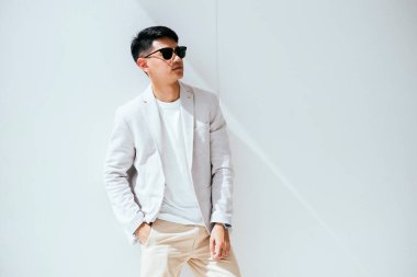 Beyaz takım elbiseli, güneş gözlüklü bir adam beyaz duvarda ışık ve gölgeli bir model gibi davranır..