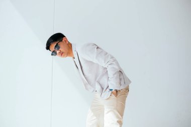 Beyaz takım elbiseli, güneş gözlüklü bir adam beyaz duvarda ışık ve gölgeli bir model gibi davranır..