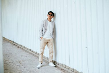 Beyaz takım elbiseli, güneş gözlüklü bir adam yokuş aşağı yürürken duvara yaslanıyor..