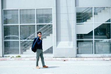 Koyu mavi gömlekli bir adam güneş ışığında gözlük binasının önünden geçiyor..