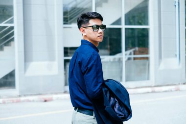 Koyu mavi gömlekli bir adam güneş ışığında gözlük binasının önünden geçiyor..