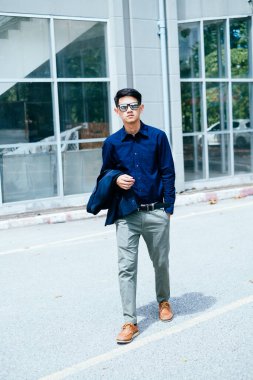 Koyu mavi gömlekli bir adam güneş ışığında gözlük binasının önünden geçiyor..