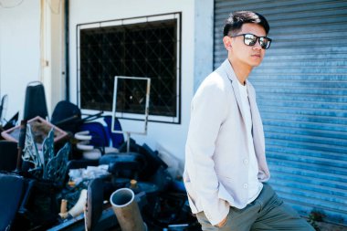 Beyaz takım elbiseli bir adam güneş gözlüğü takıyor ve iskemle çöplüğünde oturuyor..