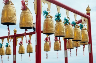 Tapınağın kırmızı yapısında küçük altın bir çan var. Arka planda bulutlu gökyüzü var..