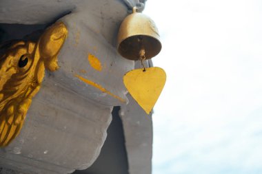 Arka planda gökyüzü olan beton ejderhanın sonundaki küçük çanı yakın plan çek..