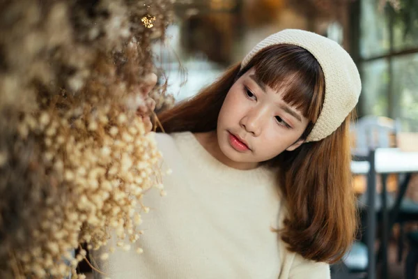 穿着米色头巾的布鲁内特姑娘站在咖啡店里的干花旁边 采暖光 — 图库照片