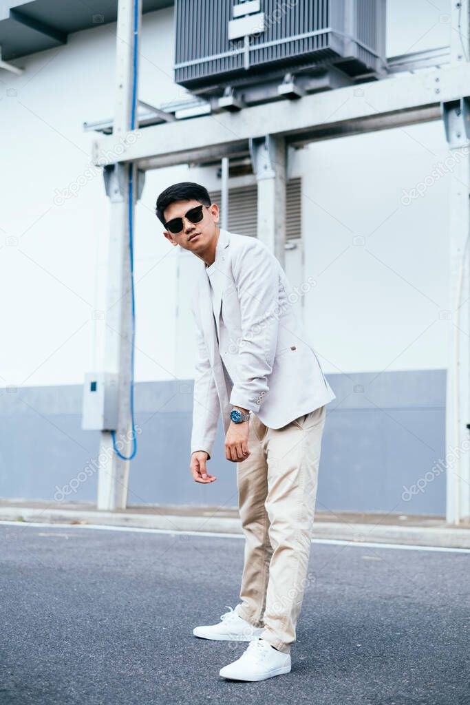 A man in white suit wearing sunglasses standing like a hunchback next to the factory.
