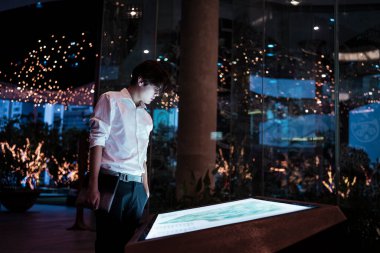 Yarı resmi giyinmiş siyah saçlı adam duruyor ve alışveriş merkezindeki ışıklı LED uyarısına bakın..