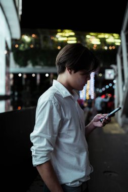 Alış veriş merkezinin önünde elinde LED reklam panosuyla duran siyah saçlı adam haritadaki yerini kontrol etmek için akıllı telefonunu tutuyor..