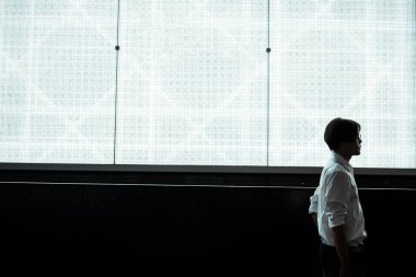 Beyaz tişörtlü, cep telefonuyla beyaz ışıklı alışveriş merkezinin reklam panosunun önünde duran adamın silüeti..