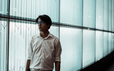 Beyaz tişörtlü, gözlüklü, siyah saçlı adam LED duvarın önünde duruyor..