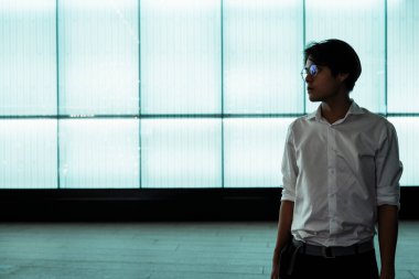 Beyaz tişörtlü, gözlüklü, siyah saçlı adam LED duvarın önünde duruyor..