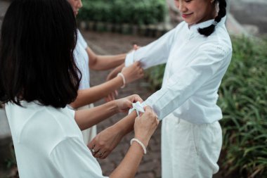 Two twin sister roll the shirt's sleeve for a pigtails girl in the park. clipart