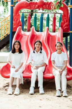 Üçlü ikiz kardeş kırmızı sürgüde yan yana oturuyor..