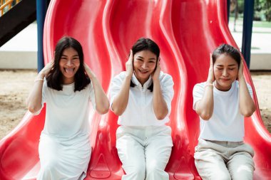 Üçlü ikiz kardeş oyun parkında kırmızı kaydırağın ucunda oturuyor, kulaklarını kapat..