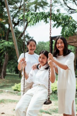 Üçlü ikiz kardeş yazın parkta salıncak oynuyor..