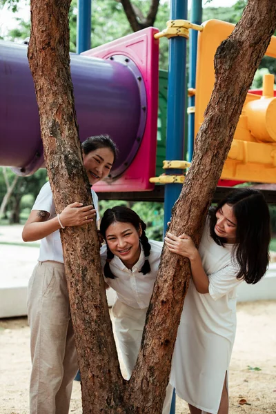 Üçlü ikiz kardeş ağaçların etrafında birlikte oynuyorlar. Oyun bahçesindeki V işareti gibi..
