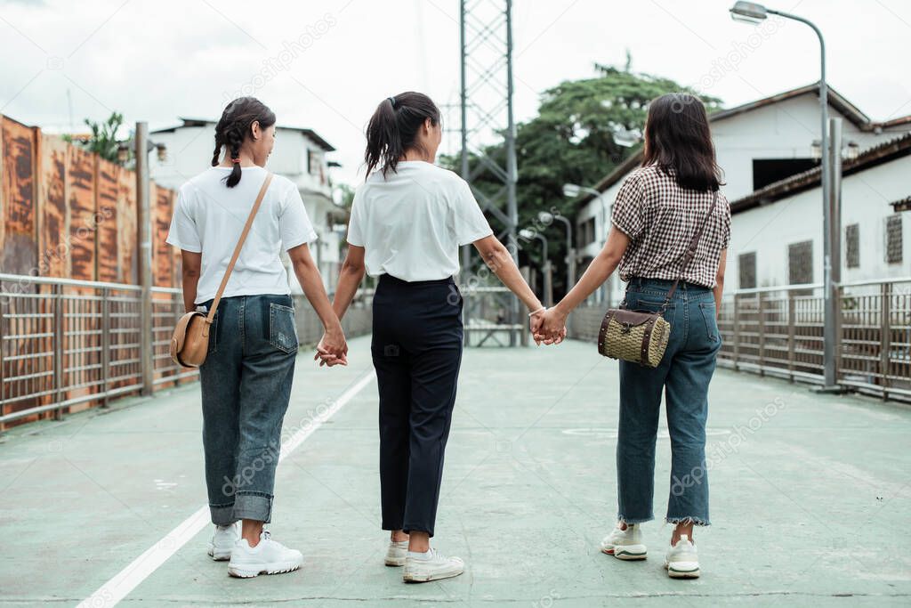 Back shot of triple twin sister holding each other hands and walking together in the town.