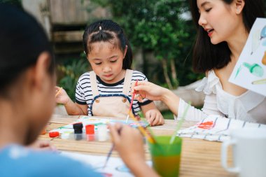 İki Asyalı kız kardeş açık havada su boyası yapıyor. Aile aktivitesi..