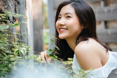 Doğada beyaz elbise giymiş güzel Asyalı bir kadının portresi. Mutluluk ifadesiyle gülümsüyor.