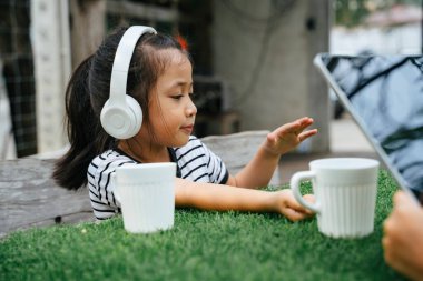 Parktaki bankta oturan küçük kız, beyaz kablosuz kulaklıkla müzik dinliyor..