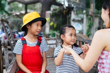 Üç kız kardeş parkta birlikte seyahat eder. Abla en küçük kız kardeşin elini tutuyor..