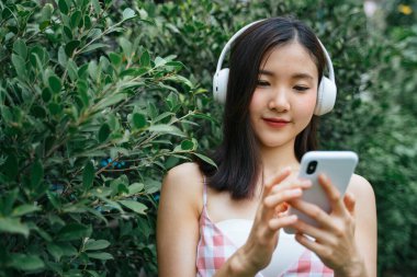 Kulaklıklı güzel genç bir kadın. Ağaç dikme duvarında dikilmiş, gözleri kapalı müzik dinliyor..