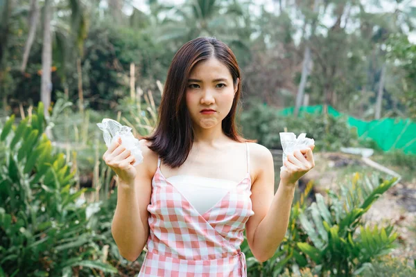 Angry furious asian girl on pink dress hating plastic bag. Save the world. Global warming. Save planet from plastic waste. Holding crumping plastic bag with two hands.