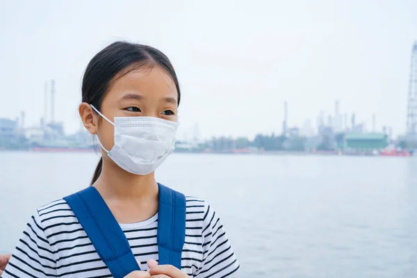 防毒观念 亚洲小女孩戴着防毒面罩 在烟雾中站在河边 到处都是污染 — 图库照片