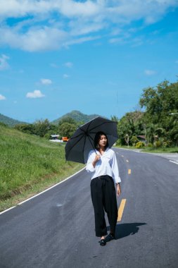 Taylandlı kadın elinde siyah şemsiyeyle ülke yolunda yürüyor..