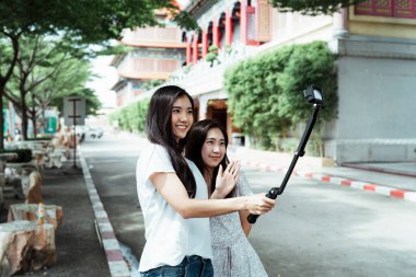 İki güzel Asyalı kadın Çin parkında selfie çubuğuyla video kaydediyor..