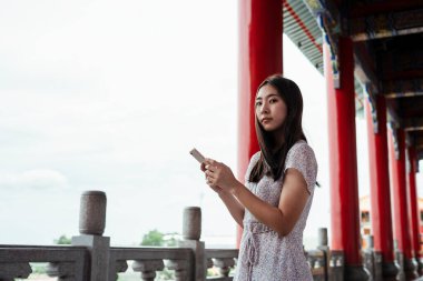 Çin büyük sarayında ya da tapınakta seyahat ederken akıllı telefon kullanan sevimli Asyalı genç bir kadın..
