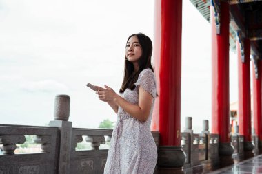 Çin büyük sarayında ya da tapınakta seyahat ederken akıllı telefon kullanan sevimli Asyalı genç bir kadın..