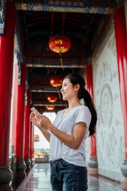 Akıllı telefonu kullanarak dünyayı tek parmakla birbirine bağlayan sevimli genç bir kadın. Çin tapınağı.