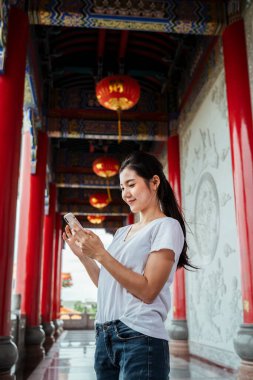 Akıllı telefonu kullanarak dünyayı tek parmakla birbirine bağlayan sevimli genç bir kadın. Çin tapınağı.
