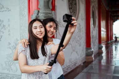 Tatlı Asyalı genç kadınlar kameralarını selfie çubuğuna yerleştiriyor, açıyı ayarlıyorlar, Çin tapınağına..