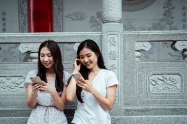 İki güzel Asyalı kadın birlikte akıllı telefon kullanıyor ve gülümsüyor. Çin tapınağında..