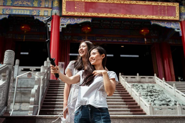 两个年轻的亚洲女人拿着自拍棒 在中国庙宇里做博客 — 图库照片