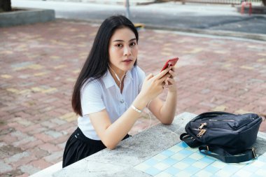 Üniformalı siyah uzun saçlı üniversiteli kız mermer masadaki müziği dinle..