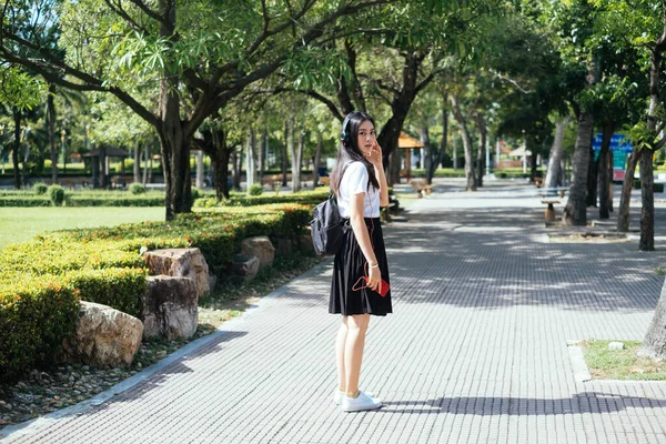 Uzun saçlı siyah üniformalı kız yürümeyi bırak ve kulaklıkla müzik dinlerken kameraya dön..