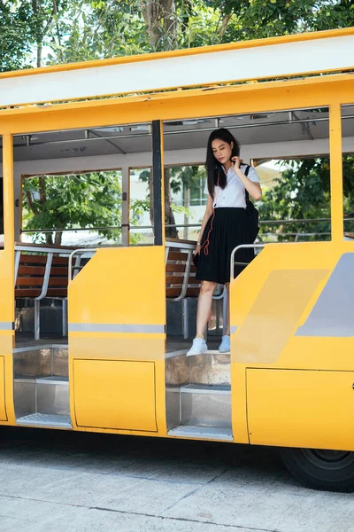 Black long hair college girl in uniform walk down the bus, get out of the yellow bus.