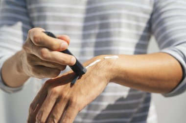 Kollarına krem sürerek deriyi ultraviyole güneş ışığından koruyan bir adamın eli. Güneş koruması. Güneş kremi şişesi. Güneş kremi insan elinin üzerinde.