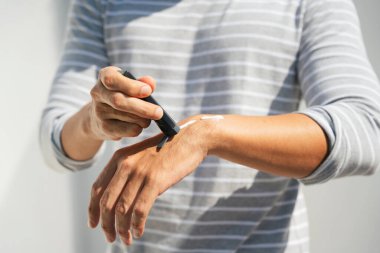 Kollarına krem sürerek deriyi ultraviyole güneş ışığından koruyan bir adamın eli. Güneş koruması. Güneş kremi şişesi. Güneş kremi insan elinin üzerinde.