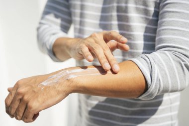 Kollarına krem sürerek deriyi ultraviyole güneş ışığından koruyan bir adamın eli. Güneş koruması. Güneş kremi şişesi. Güneş kremi insan elinin üzerinde.